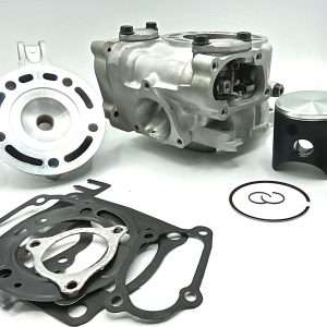 Disassembled engine parts including a cylinder head, gaskets, piston, and rings laid out on a white surface in a workshop setting.